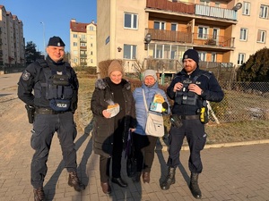 Dwaj policjanci oraz dwie starsze kobiety z prezentami w rękach pozujący na tle bloku