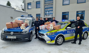 Dwa radiowozy, na których leżą prezenty oraz grupka policjantów przed budynkiem