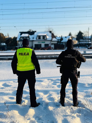 W scenerii zimowej policjant stojący przy torach policjant oraz strażnik ochrony kolei