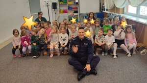 Uśmiechnięty policjant pozujący do zdjęcia wraz z przedszkolakami w sali