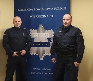 Dwaj policja pozujący do zdjęcia na tle baneru jednostki