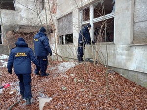 Policjant zaglądający przez otwór okienny do pustostanu, za nim dwójka strażników miejskich, sceneria zimowa