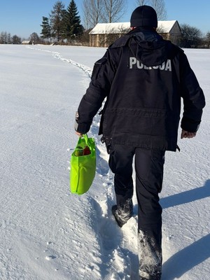 Policjant z siatką przedzierający się przez ośnieżone pole w kierunku zabudowań