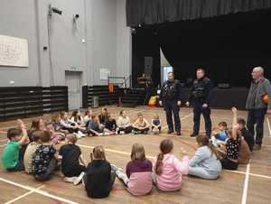 Dwaj policjanci podczas pogadanki dla dzieci zgromadzonych w kręgu na sali gimnastycznej