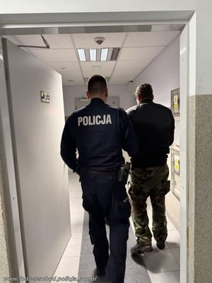 Widziani z tyłu w korytarzu komisariatu: policjant prowadzący mężczyznę