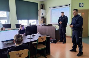 Dwaj policjanci podczas prelekcji dla dzieci w sali komputerowej