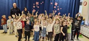 Grupa przedszkolaków pozująca do zdjęcia z policjantem w sali