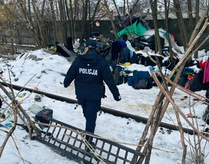 W scenerii zimowej otwarta przestrzeń z pryzmą szmat i idąca w tym kierunku policjantka
