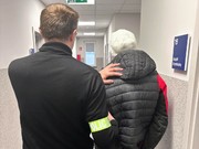 Widziani z tyłu w korytarzu komisariatu policjant oraz mężczyzna w zimowej kurtce