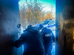 Policjant wyprowadzający ze zrujnowanego budynku starszego mężczyznę