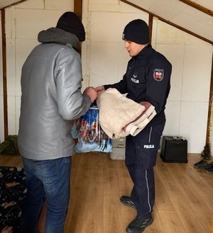 Wewnątrz pomieszczenia gospodarczego policjant wręczający paczkę starszemu mężczyźnie