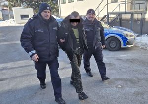 Dwaj policjanci prowadzący mężczyznę przez dziedziniec komendy