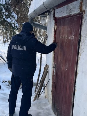 Policjant w scenerii zimowej pukający do starych drewnianych drzwi chatki