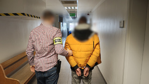 W korytarzu urzędu policjant po cywilnemu przytrzymujący mężczyznę ze skutymi rękami