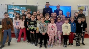 Grupa przedszkolaków wewnątrz sali pozująca do zdjęcia z dwoma policjantami