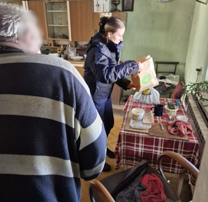 Wewnątrz mieszkania policjantka wykładająca artykuły spożywcze na stół oraz starszy męzczyzna