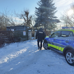 W scenerii zimowej policjant idący od radiowozu w kierunku blaszanego budynku