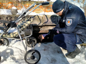 W scenerii zimowej policjant kucający przy otworze ziemianki z widoczną sylwetką mężczyzny