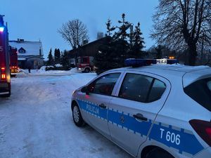 W scenerii zimowej zabudowania, radiowóz i wozy strażackie