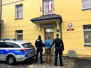Dwóch policjantów przytrzymujących mężczyznę przed wejściem do komisariatu