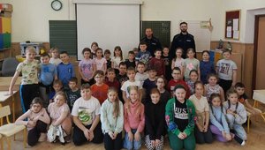 Dwóch policjantów z grupą dzieci pozujący do zdjęcia w sali szkolnej