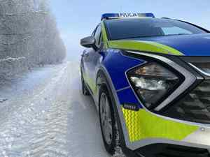 Widziany z dołu radiowóz w scenerii zimowej stojący na drodze wzdłuż lasu