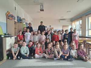 W sali przedszkolnej grupa przedszkolaków oraz dwójka policjantów pozujących do zdjęcia