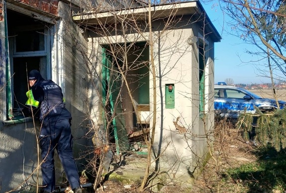 Policjant zaglądający przez otwór okienny do wnętrza zrujnowanego budynku