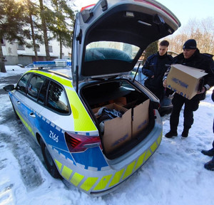 W scenerii zimowej dwaj policjanci wkładający kartony do bagażnika radiowozu