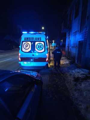 W scenerii zimowej nocy karetka pogotowia stojąca przy kamienicy a obok policjant