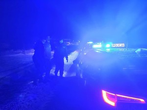 W scenerii zimowej, nocą droga i dwóch policjantów prowadzących mężczyznę do radiowozu