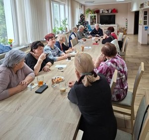 Seniorzy siedzący przy długim stole konferencyjnym oraz policjantka prowadząca prelekcję