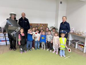 Trójka policjantów pozująca do zdjęcia z grupą przedszkolaków wewnątrz sali