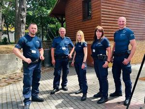 Piątka uśmiechniętych policjantów w scenerii letniej na tle drewnianego domku