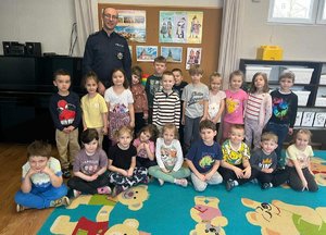 Uśmiechnięty policjant pozujący z grupą przedszkolaków do zdjęcia w sali