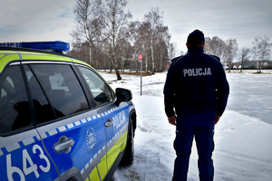 W scenerii zimowej policjant obok radiowozu nad brzegiem zamarzniętego zbiornika wodnego