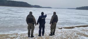 Widziani z tyłu nad brzegiem akwenu wodnego w scenerii zimowej policjant i dwaj mężczyźni w strojach typu moro