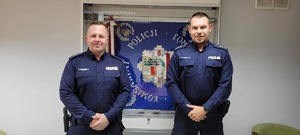 Dwóch policjantów na tle gabloty ze sztandarem policji