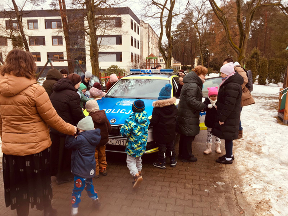 Grupa dzieci i wychowawczyń obok radiowozu zaparkowanego na ulicy w scenerii zimowej