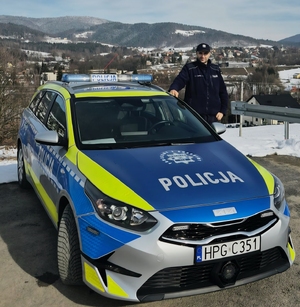 Policjant obok radiowozu na tle ośnieżonych gór