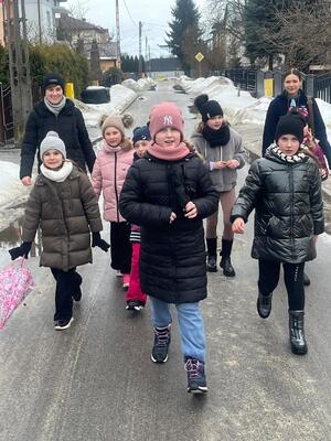 Grupa dzieci z dwiema kobietami idących ulicą w scenerii ziomowej