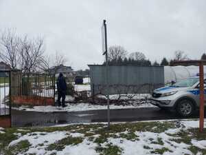 Policjant przy ogrodzeniu działki z blaszanym garażem, obok radiowóz