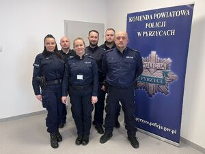 Grupa uśmiechniętych policjantek i policjantów na tle baneru KPP w Pyrzycach