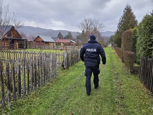 Policjant idący przez kompleks ogródków działkowych