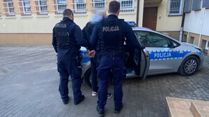 Dwaj policjanci na dziedzińcu komisariatu wsadzający zatrzymanego do radiowozu