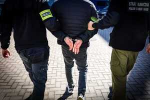 Widziani z tyłu policjant i strażnik graniczny prowadzący skutego mężczyznę