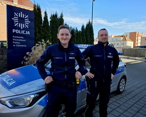 Dwójka uśmiechniętych policjantów na tle radiowozu