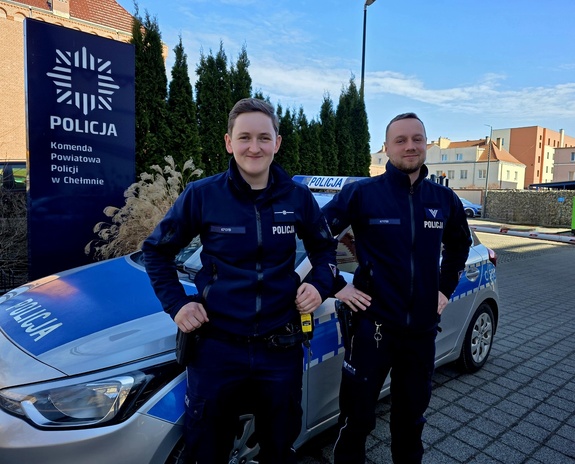 Dwójka uśmiechniętych policjantów na tle radiowozu