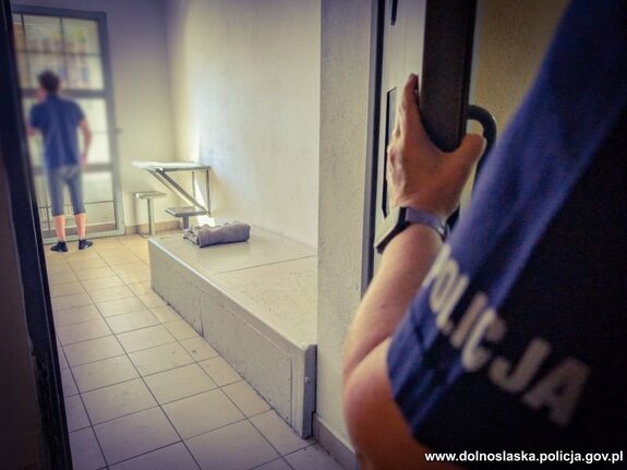 Mężczyzna wewnątrz celi oraz policjant stojący przy drzwiach celi