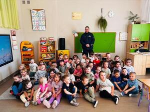 Policjant pozujący wewnątrz sali do zdjęcia z grupą siedzących przedszkolaków